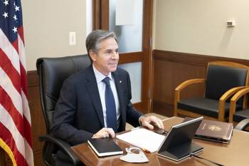 United States Secretary of State Anthony Blinken sits at a desk in front of an American flag.